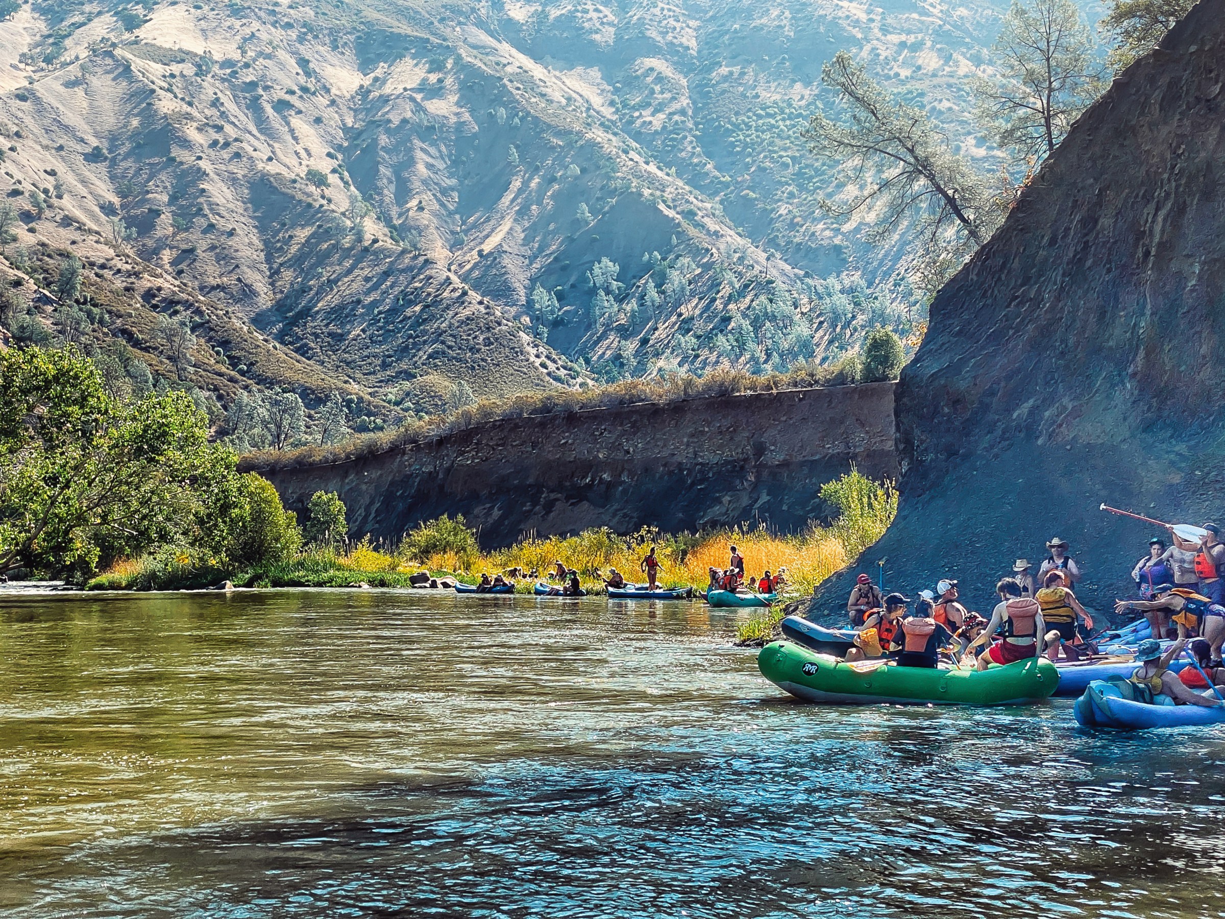 Groups of people rafting on a river surrounded by mountains and trees.